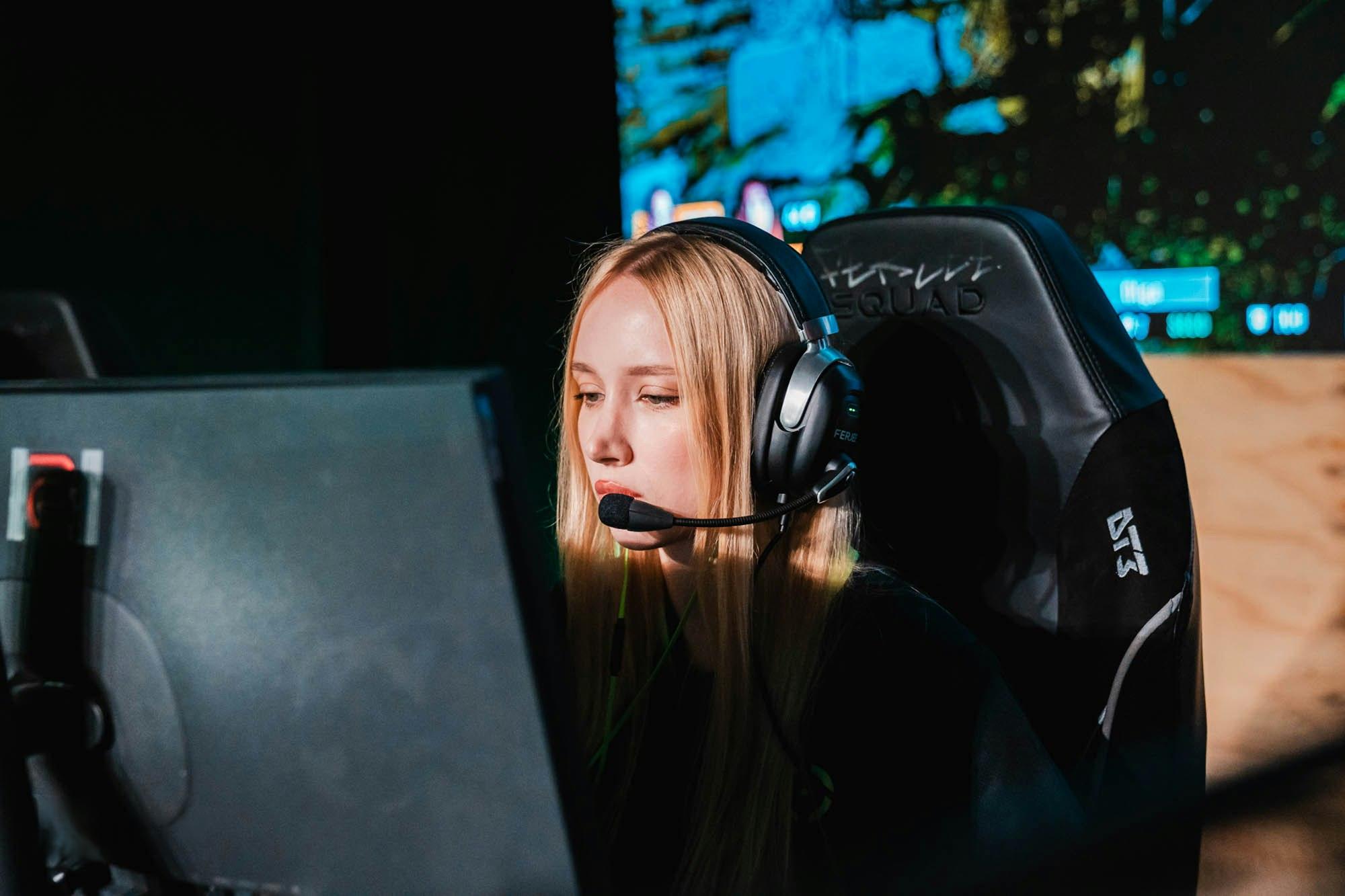 Jugadora profesional con auriculares concentrada frente a su monitor en un escenario de esports